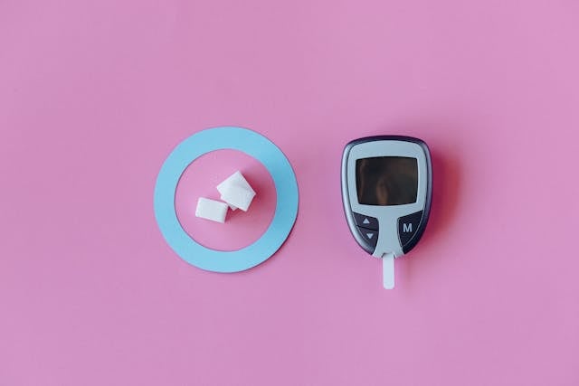 Energy Homeostasis: How Your Body Works to Balance Energy 7 A glucose meter and sugar cubes on a turquoise plate against a pink background.