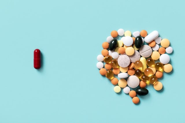 NAD vs Niacin vs Niacinamide: Vitamin B3 Differences Decoded 4 A single red capsule sits apart from a large pile of various colorful pills and supplements.