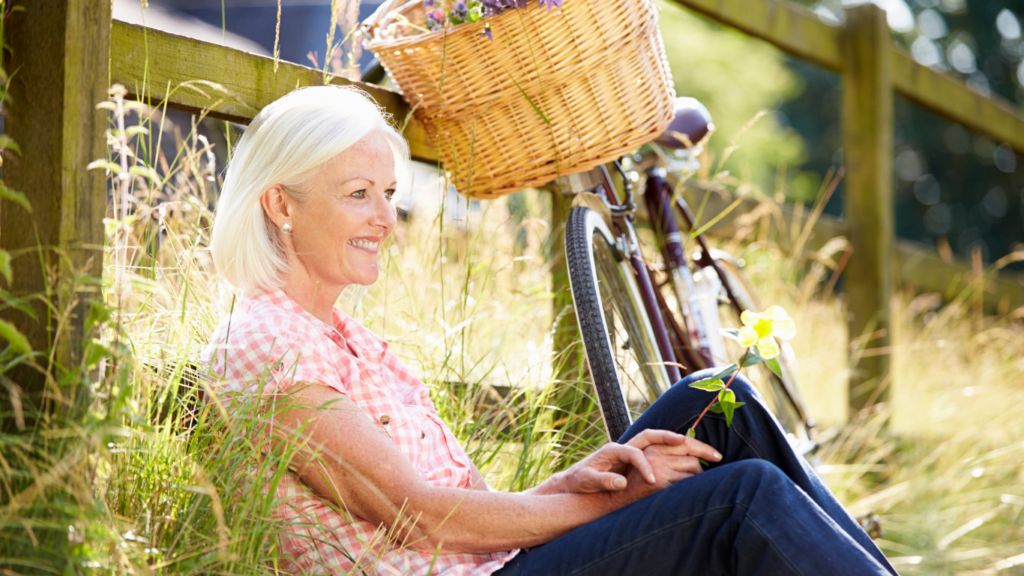 An older woman on a bike ride taking a pause at a fence to take in the countryside beauty