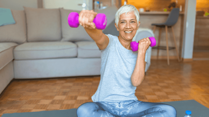 5 Anti-Inflammatory Health Benefits of Ginger Root 5 A woman sitting on a yoga mat, holding pink dumbbells in both hands.