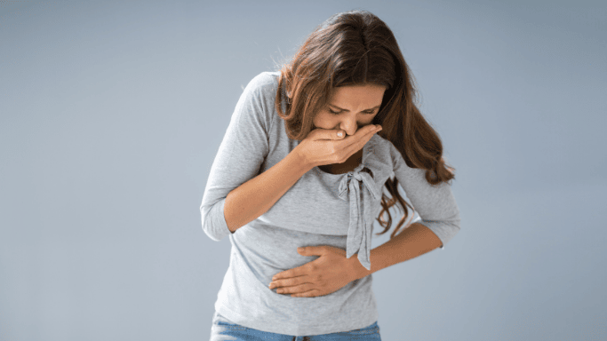 5 Anti-Inflammatory Health Benefits of Ginger Root 7 A woman holding her stomach with her left hand and covering her mouth with her right hand, appearing to vomit.