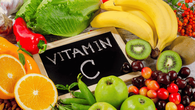 Can Vitamin C and Zinc Prevent or Shorten Your Cold? 4 An image showing vitamin C-rich foods displayed on a table, including oranges, banana, kiwi, bell peppers, and leafy greens.