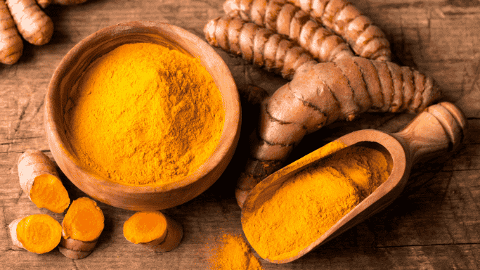 An image showing fresh turmeric roots and turmeric powder in wooden bowl.