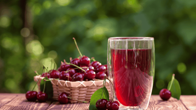 An image showing a glass of cherry juice placed in front, with fresh cherries in a basket slightly behind and to the side.