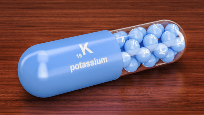 10 Vitamins and Minerals with Anti-Aging Benefits 13 A blue capsule pill labeled with the chemical element potassium containing smaller blue spheres inside, each also marked with the letter "K."