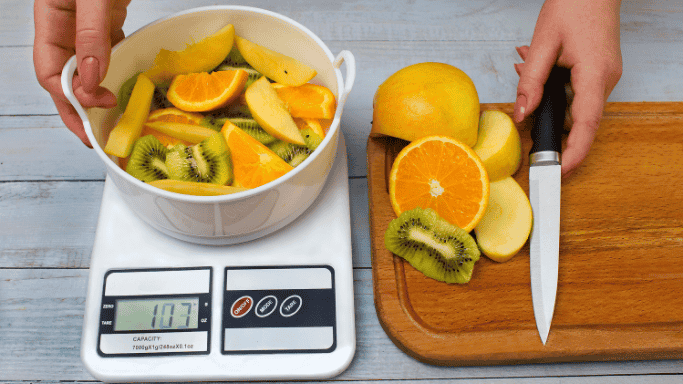 Can Vitamin C Help You Lose Weight? 5 An image of assorted cut fruits placed on a kitchen weighing scale, symbolizing healthy eating, portion control, or balanced nutrition.