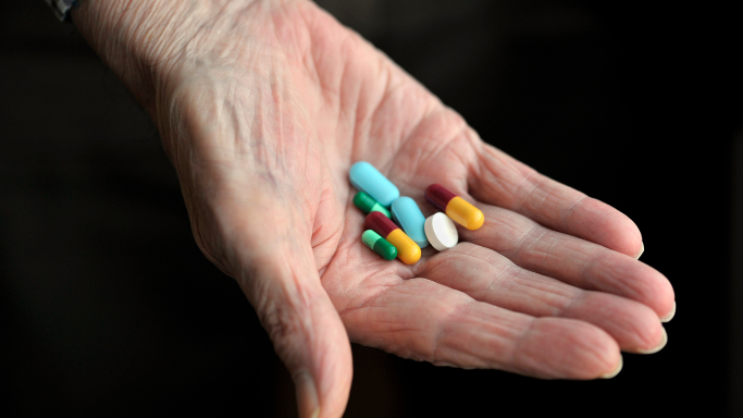 Niacin (B3): Side Effects, Reactions, Overdose Risks Explained 10 An elderly hand holding various colorful pills and capsules.
