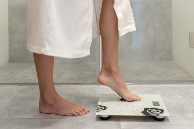 A person in a white towel steps onto a digital bathroom scale with bare feet.