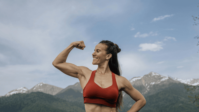 Glutamine vs Creatine: Science-Based Comparison 5 Athletic woman flexing her bicep outdoors, representing the muscle-building and strength-enhancing benefits of creatine supplementation.