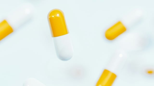 How to Take Turmeric: Dosage, Timing & Absorption Tips 4 Yellow and white turmeric capsules falling against a light blue background.