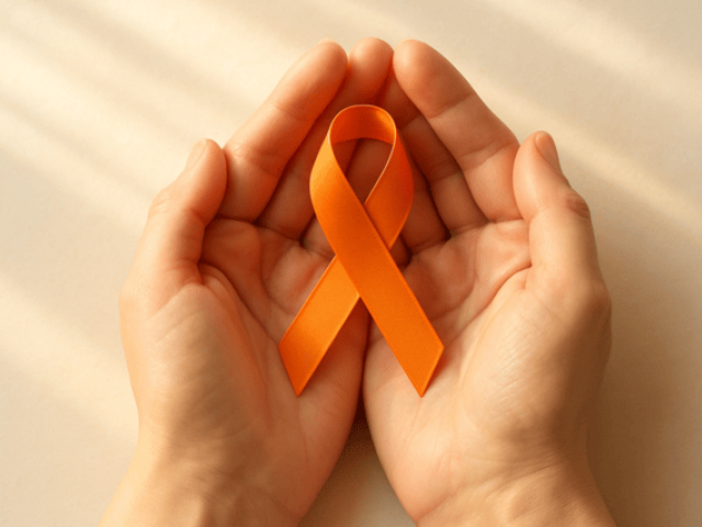 Two cupped hands protectively hold an orange multiple sclerosis awareness ribbon against a light background.