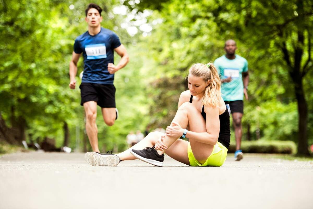 Female runner in black and yellow athletic wear sits on path holding injured leg.
