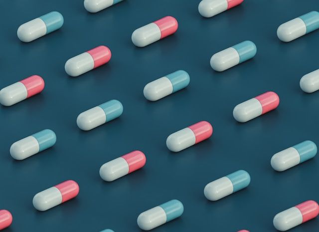 Pink and blue capsules arranged in a repeating pattern on a teal background.