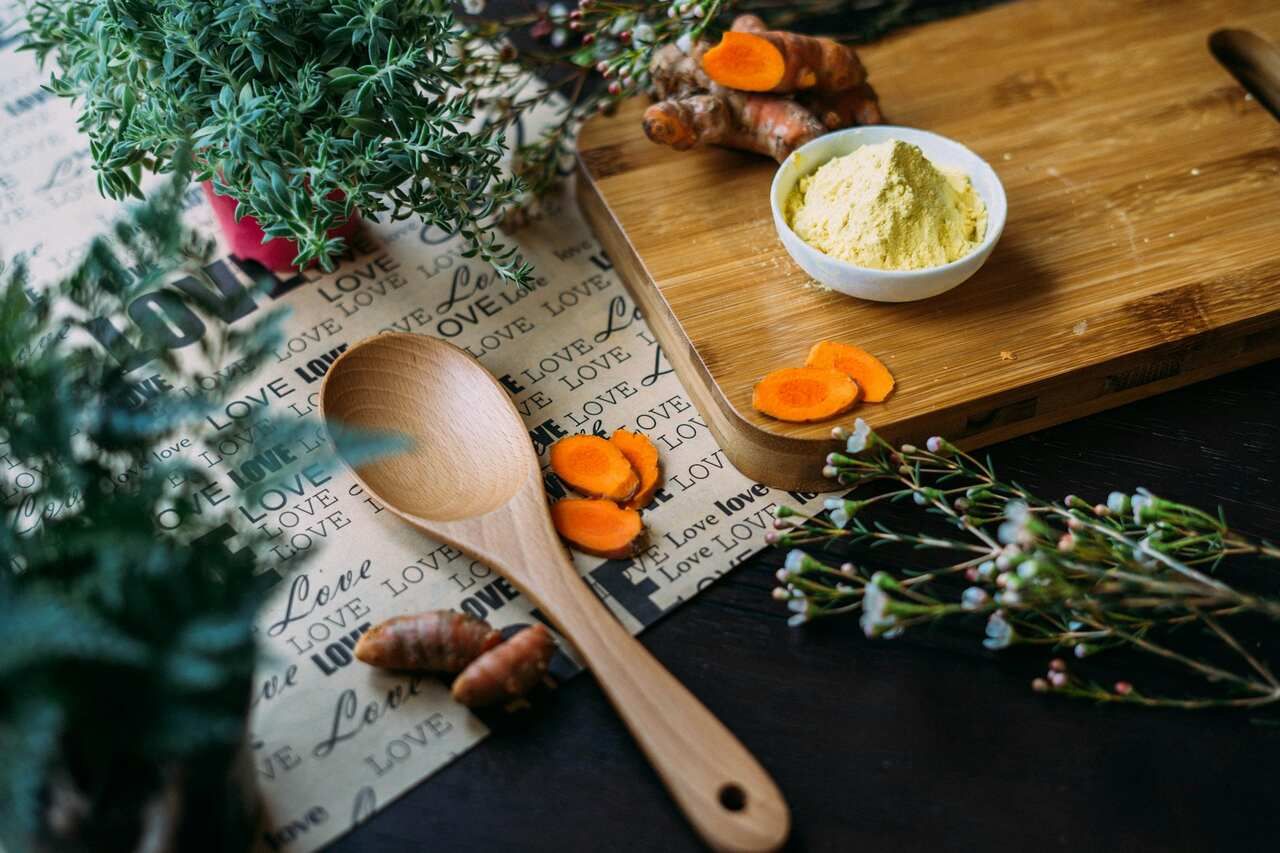 Slices of turmeric root and powder on a cutting board with green herbs