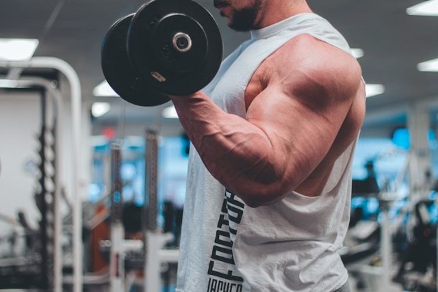 Man in white tank top lifting a black dumbbell.
