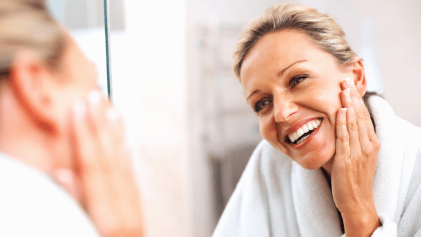 An image of a woman looking at the mirror applying skin care