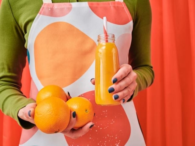 Reviewing Andrew Huberman's Supplement Routine in 2025 10 A woman in a green sweater holds fresh oranges and orange juice in a glass bottle.