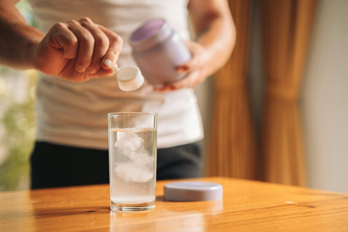 A man scooping creatine powder into a glass of water