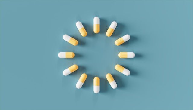 White and yellow capsules are arranged in a perfect circle pattern on a soft blue background.