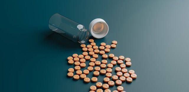 Metformin tablets spill from a clear glass bottle onto a blue-gray surface.