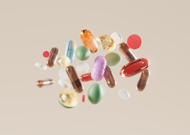 A variety of colorful pills, capsules, and tablets floating against a neutral beige background.