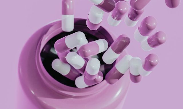 Pink and white capsules spill from a dark circular container onto a matching pink surface.