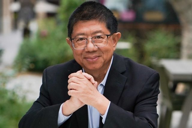 A photo of Dr. Jin-Xiong She, genomic medicine expert, seated outdoors with his hands clasped