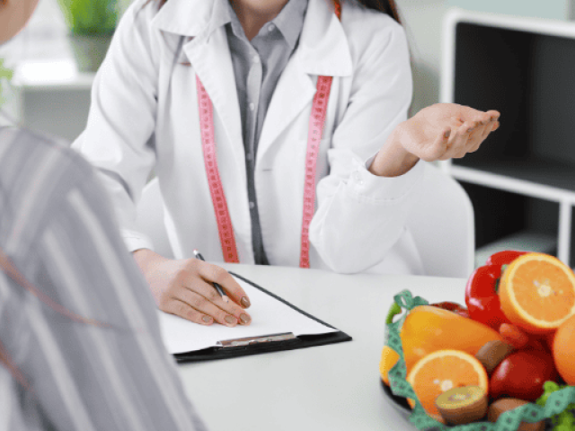 Reviewing Dr. David Sinclair's Supplement Regimen in 2025 6 A healthcare professional consults with a patient about diet and health. A bowl of vitamin C-rich fruits sits prominently on the desk, symbolizing the role of nutrition in weight management.