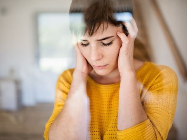 Woman in yellow sweater holding her temples with both hands, eyes closed, experiencing neuropathy and nerve pain.