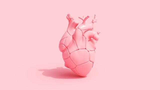 A stylized pink anatomical heart with geometric facets sits on a soft pink background surface.