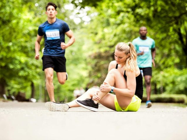 Female runner in black and yellow athletic wear sits on path holding injured leg.