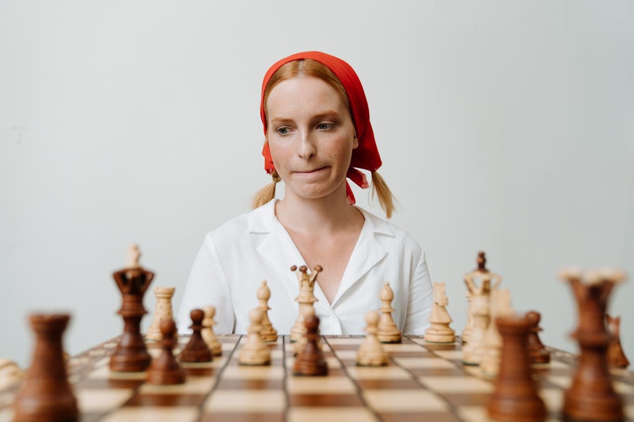 Woman staring at wooden chess board, contemplating her next move