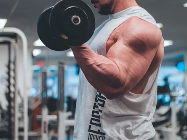 Creatine HCl vs Monohydrate: The Science-Backed Comparison 7 Man in white tank top lifting a black dumbbell.