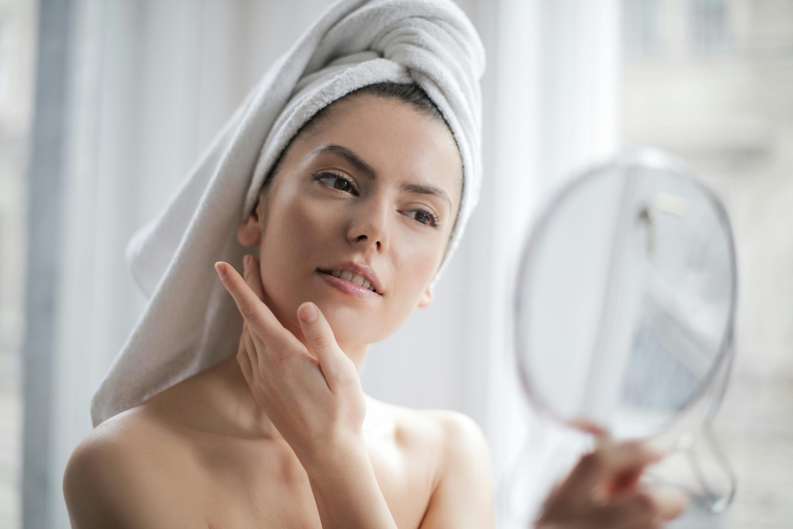 A young woman examines her skin in a handheld mirror