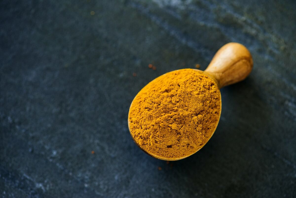A wooden scoop of turmeric powder on a marble counter.