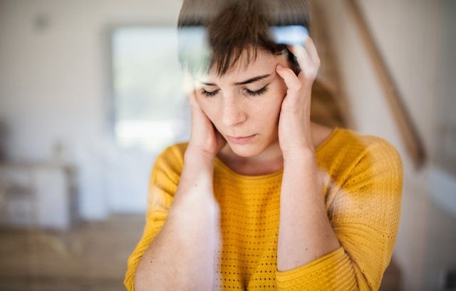 Woman in yellow sweater holding her temples with both hands, eyes closed, experiencing neuropathy and nerve pain.