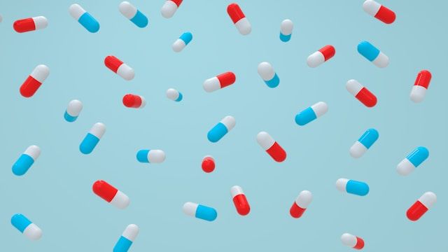 Colorful red, blue and white capsule pills are scattered randomly across a light blue background.