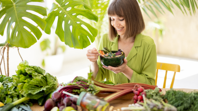An image of a Woman enjoying a bowl of vegetables surrounded by fresh, leafy greens, boosting her glutathione levels naturally.