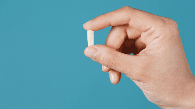 A hand holding a supplement capsule against a blue background