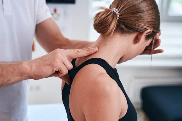 A therapist's hands work on a woman's neck and shoulder during a massage treatment.