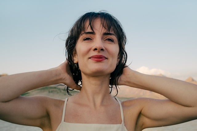 What to Expect Before and After Taking NMN Supplements 4 A smiling woman with wet hair poses with arms raised outdoors looking into the horizon.