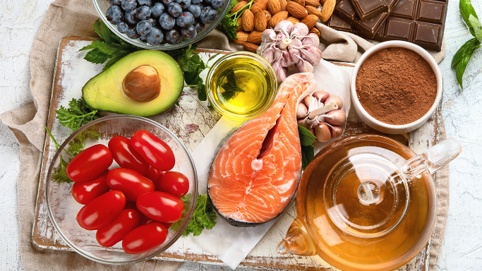 An image showing a variety of anti-aging foods, including fruits, dark chocolate, nuts, avocado, fish, and tea.