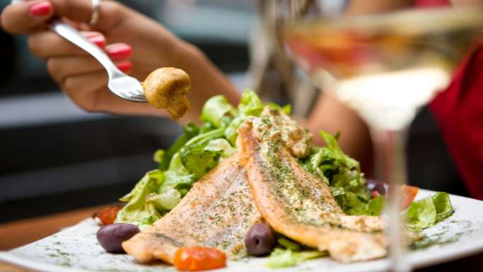 An showing a woman eating a salmon salad with mixed greens, olives, and mushrooms.