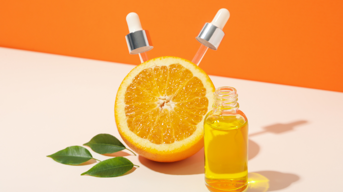 An image showing a halved orange with droppers and a bottle of vitamin C serum.