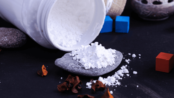 White creatine powder spilled from a container onto a stone surface. 