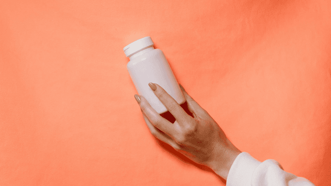 A hand holding a plain white supplement bottle against a vibrant orange background.