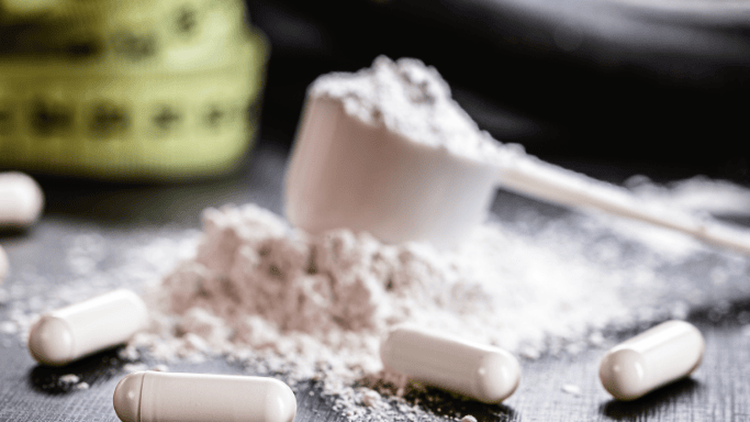 An image of creatine powder in a scoop with supplements in front
