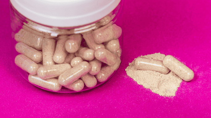 Clear jar filled with supplements against a pink backdrop