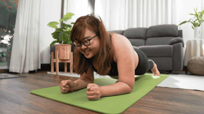 Woman doing a plank exercise on a green yoga mat indoors.