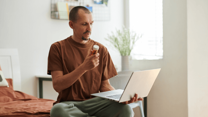 An image of a man facing his laptop with supplements